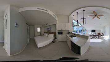 Une chambre d’hôtel moderne avec un aménagement aux lignes courbes, un lit, une kitchenette et un ventilateur de plafond.