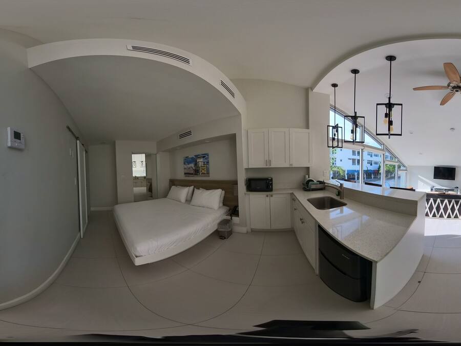 Une chambre d’hôtel moderne avec un aménagement aux lignes courbes, un lit, une kitchenette et un ventilateur de plafond.