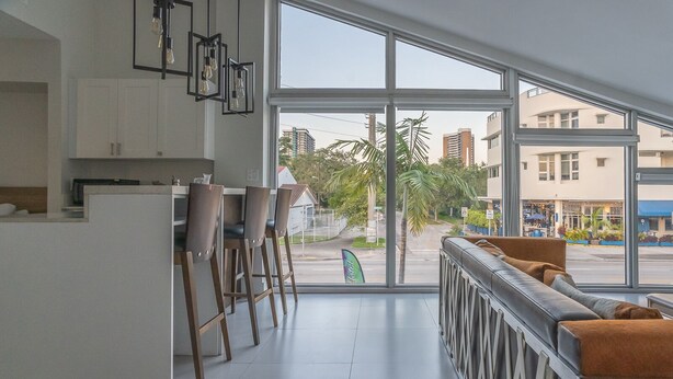 Eine moderne Küche mit weißen Schränken, einer Bar mit Barhocker und einem großen Fenster mit Blick auf die Straße und die Gebäude.