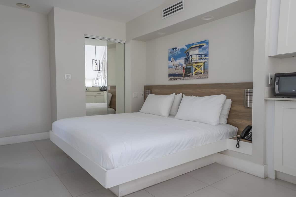 Quarto moderno com uma cama grande, cabeceira de madeira, televisão e uma obra de arte com tema de praia na parede.