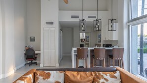 Ein modernes Wohnzimmer mit einer Couch, einem Essbereich mit Stühlen, einer Küche mit einer Arbeitsplatte und einem Deckenventilator.