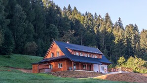 A wooden house with a sloped roof, surrounded by a grassy area and dense forest. - Hutisko - Solanec Mha555 (Hutisko-Solanec)