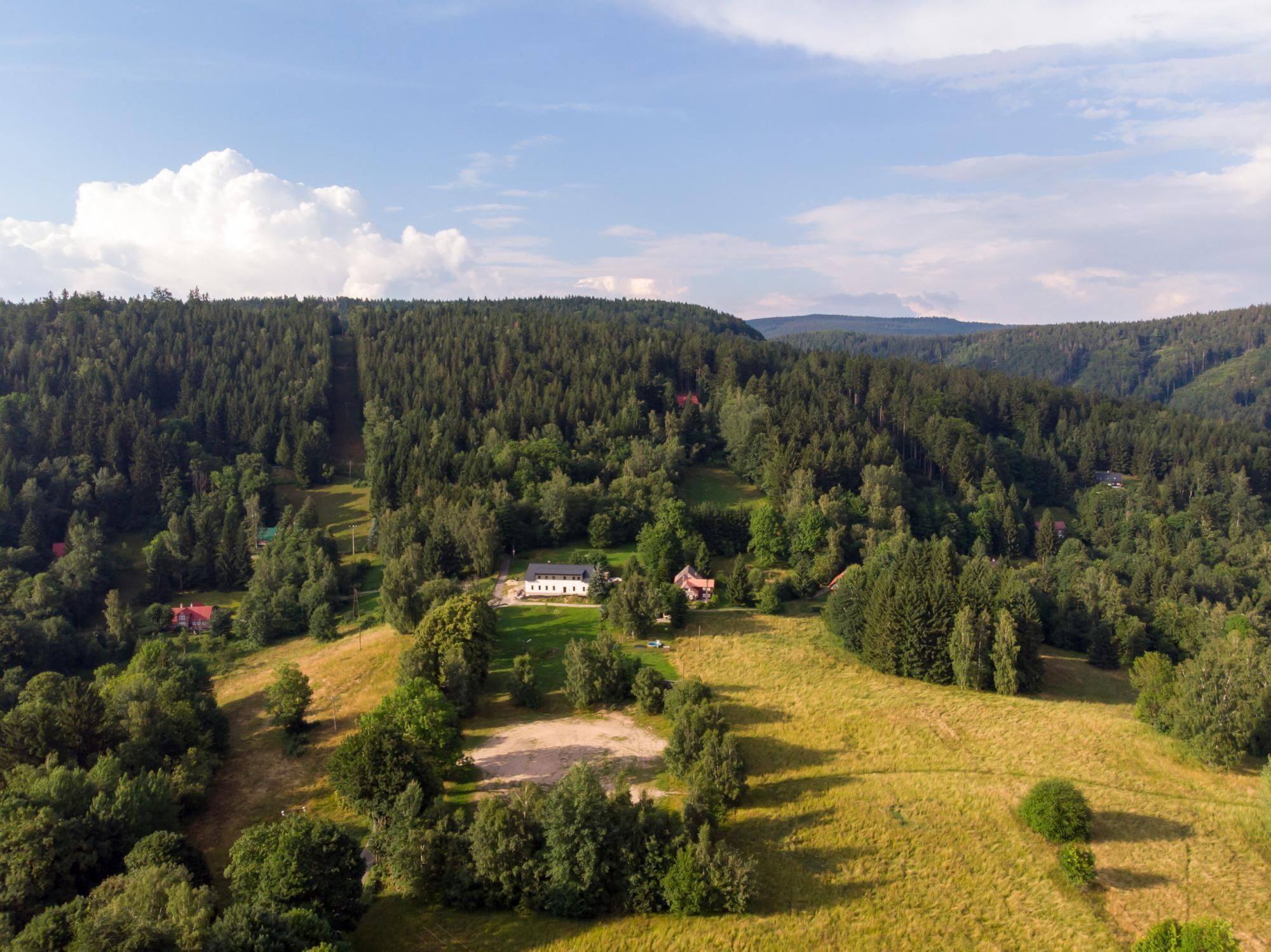 A rural landscape with a large house surrounded by dense forest and rolling hills.