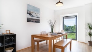 A modern dining area with a wooden table and benches, a painting on the wall, and a view through a large window. - Villa Desna - Lds021 (Desna)