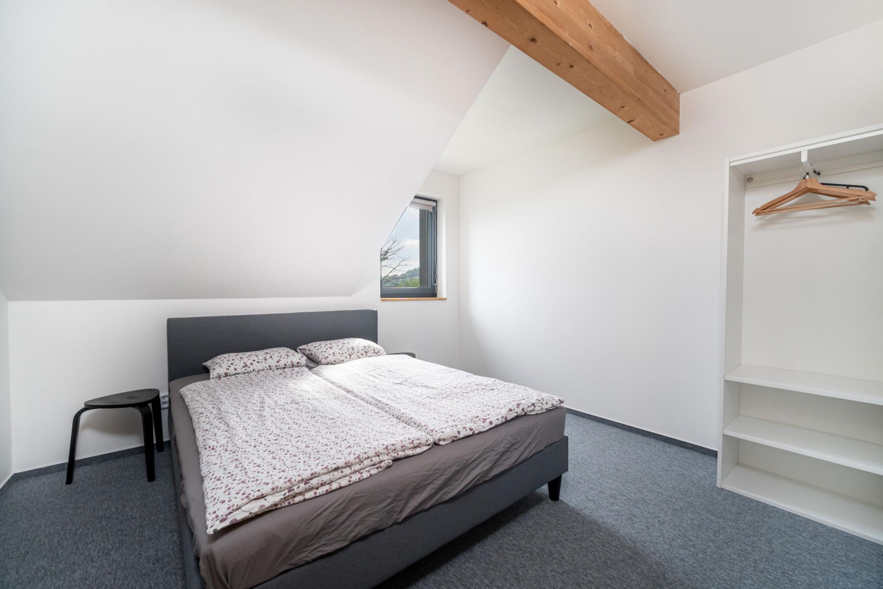 Un dormitorio con cama, un taburete, una ventana y un armario con espacio para colgar.