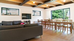 A modern living room with a sofa, dining table, chairs, and large windows offering a view of greenery. - Villa Desna - Lds021 (Desna)