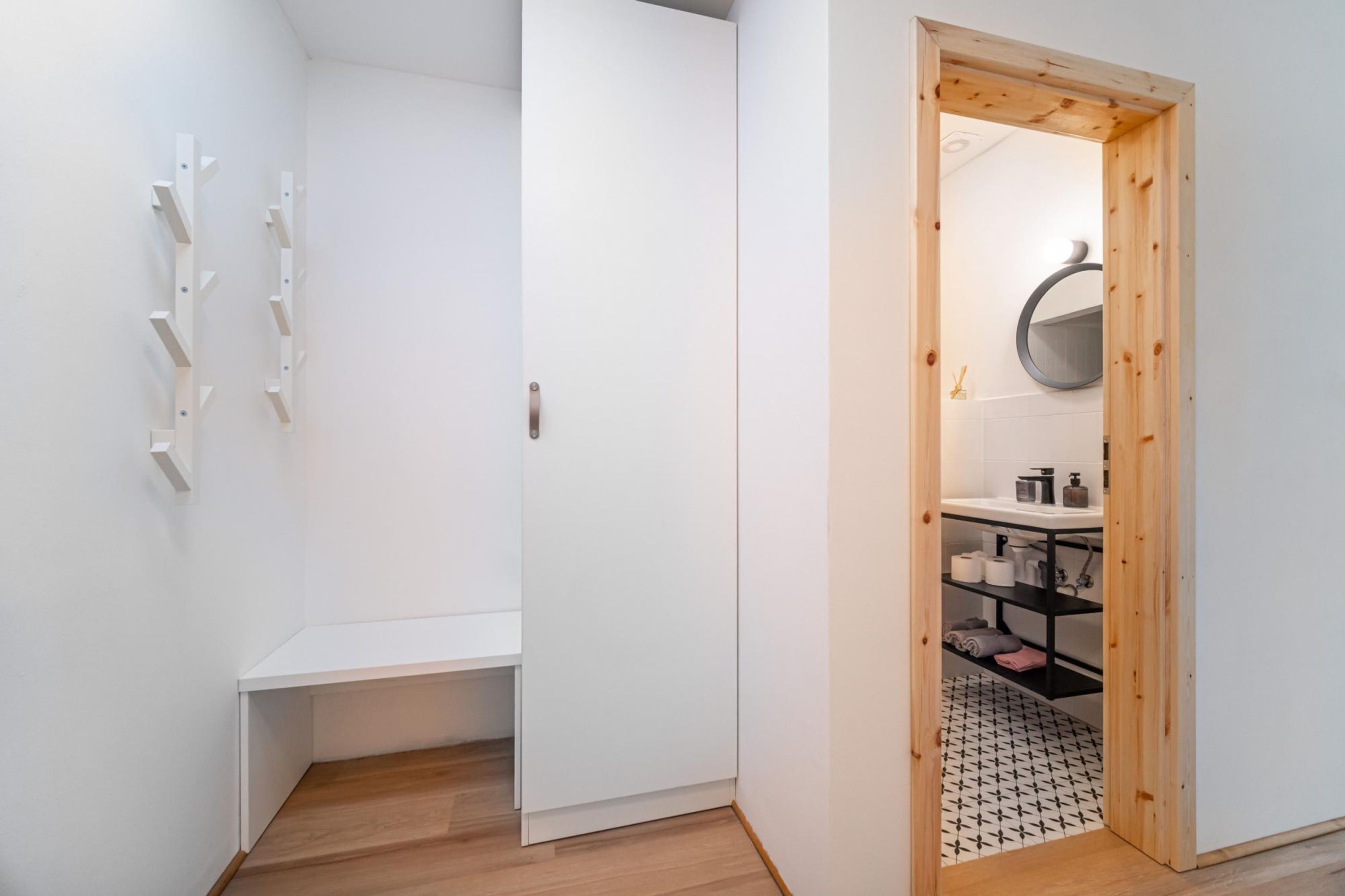 A minimalist bathroom with a white door, wooden shelves, and a tiled floor.