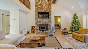 A spacious living room with a stone fireplace, a large TV mounted above it, and a Christmas tree. - Newly Renovated mountain top Ski House - Short Walk to Slopes (Somerset)