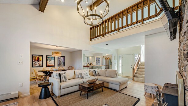 A spacious living room with a large sofa, a coffee table, and a dining area with chairs. There is a staircase leading to an upper level with a wooden railing. - Newly Renovated mountain top Ski House - Short Walk to Slopes (Somerset)