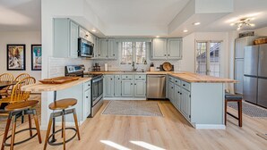 A modern kitchen with light blue cabinets, a wooden island, stainless steel appliances, and a dining area with wooden chairs. - Newly Renovated mountain top Ski House - Short Walk to Slopes (Somerset)