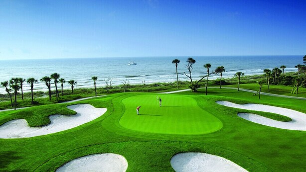 Un parcours de golf avec des bunkers de sable, une personne jouant au golf et une vue sur l’océan.