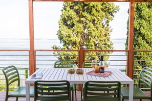 Une table dressée pour deux personnes, avec vue sur l’eau, entourée de chaises vertes, sur une terrasse en bois.
