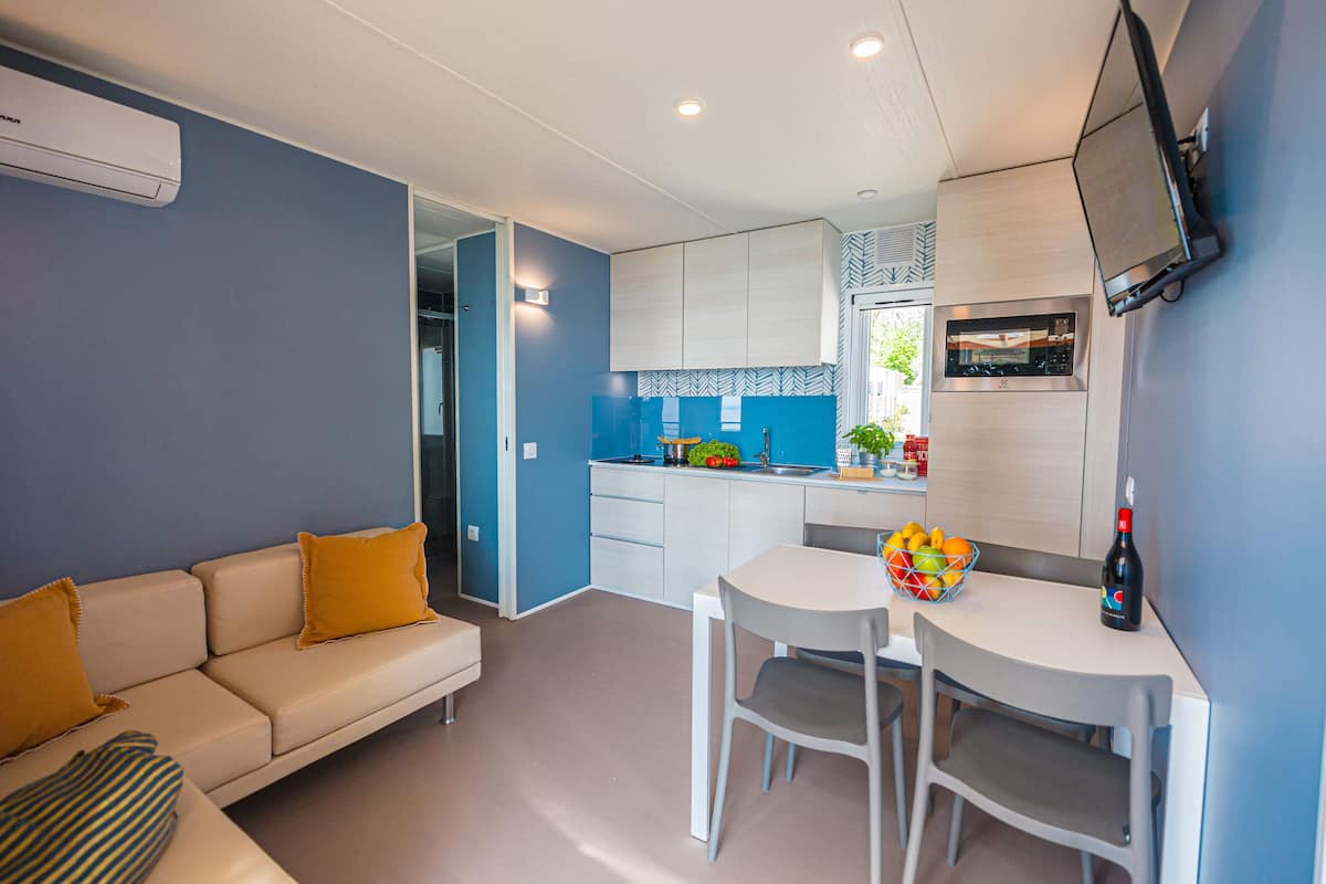 Un espacio habitable compacto con kitchenette, comedor y sofá con cojines.