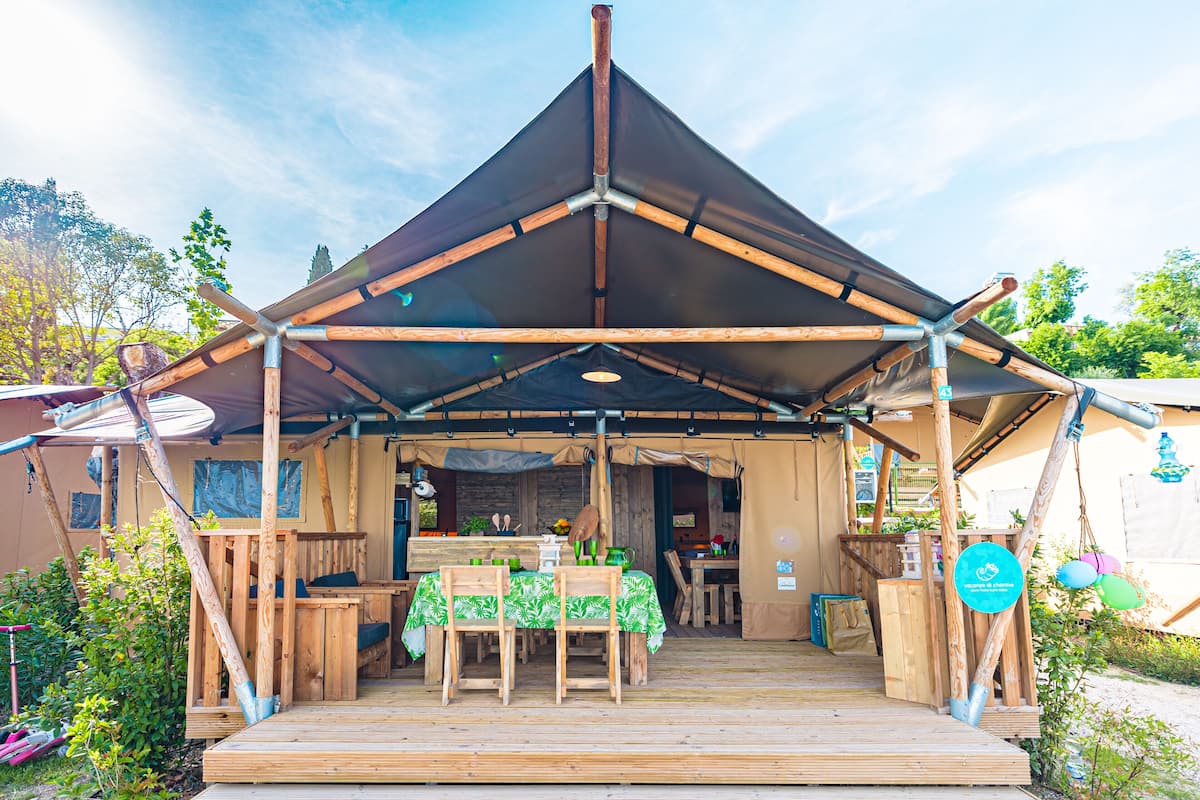 Una terraza de madera con una mesa y sillas, un área de estar cubierta y vistas al entorno verde.