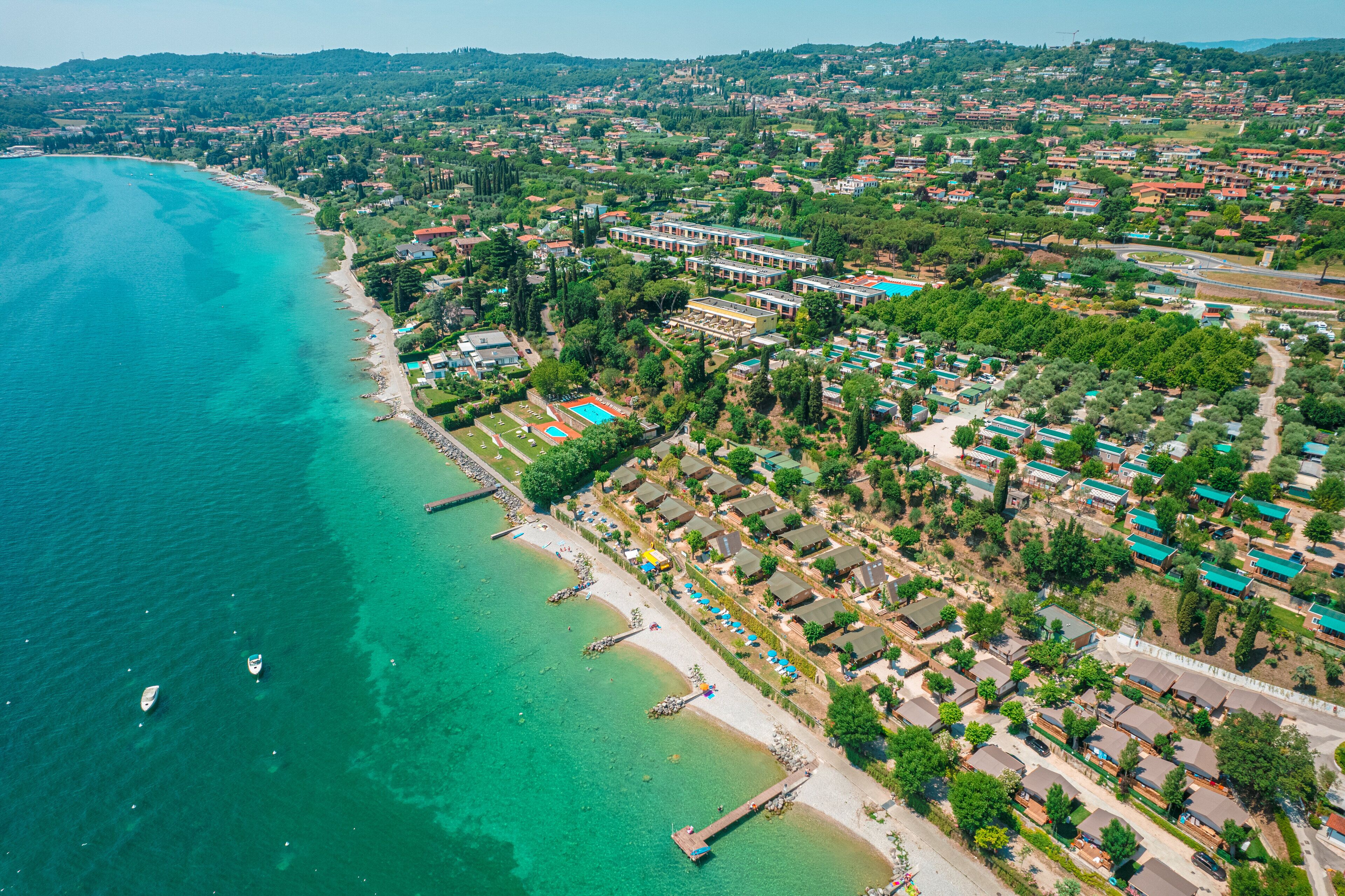 Luftaufnahme einer Küstenlandschaft mit Strand, Wohngebäuden und einem Schwimmbadkomplex.