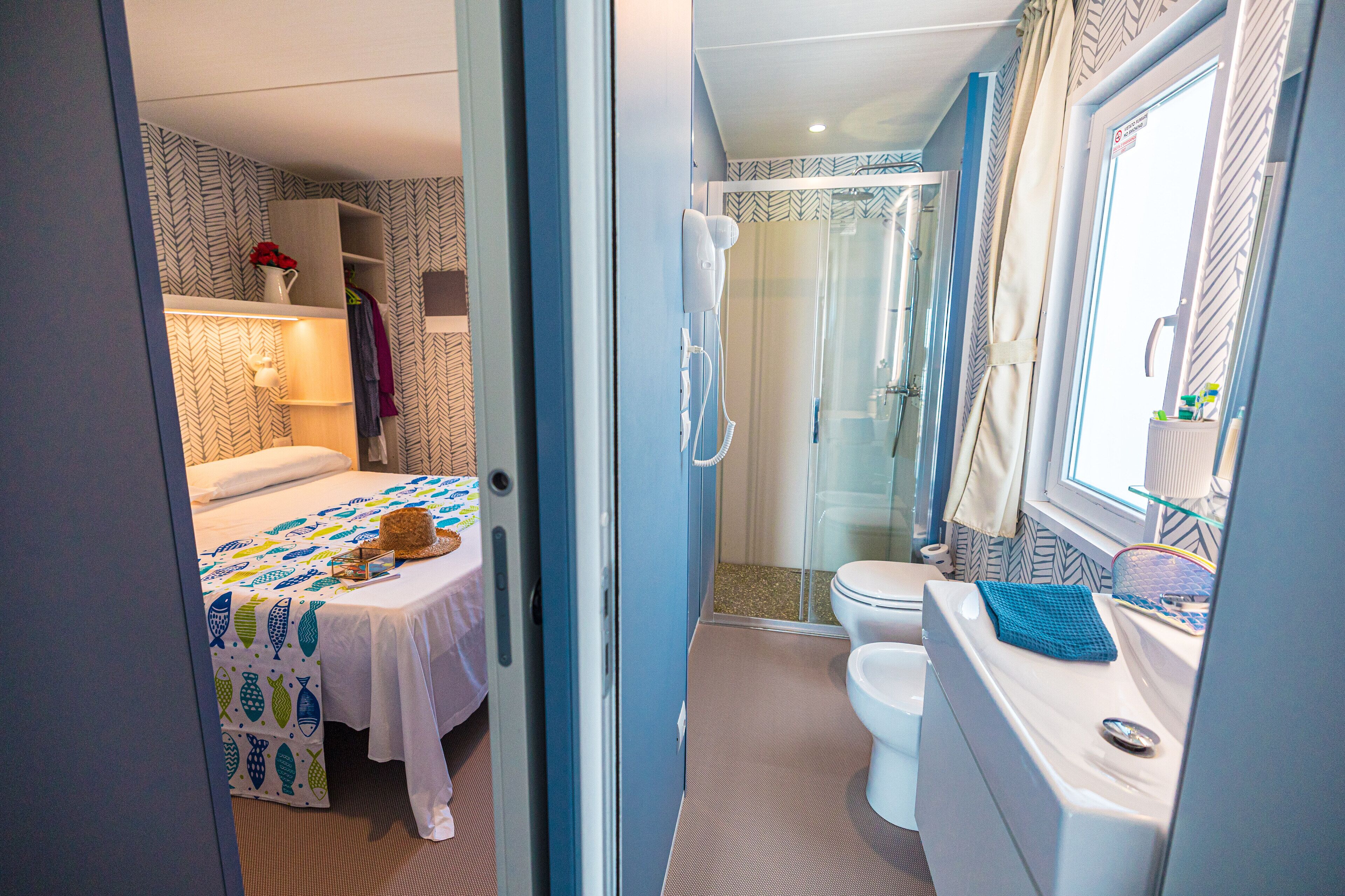 A compact bedroom with a bed, bedside table, and a small table with a vase of flowers.
