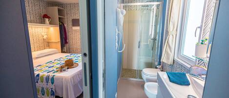 A compact bedroom with a bed, bedside table, and a small table with a vase of flowers.