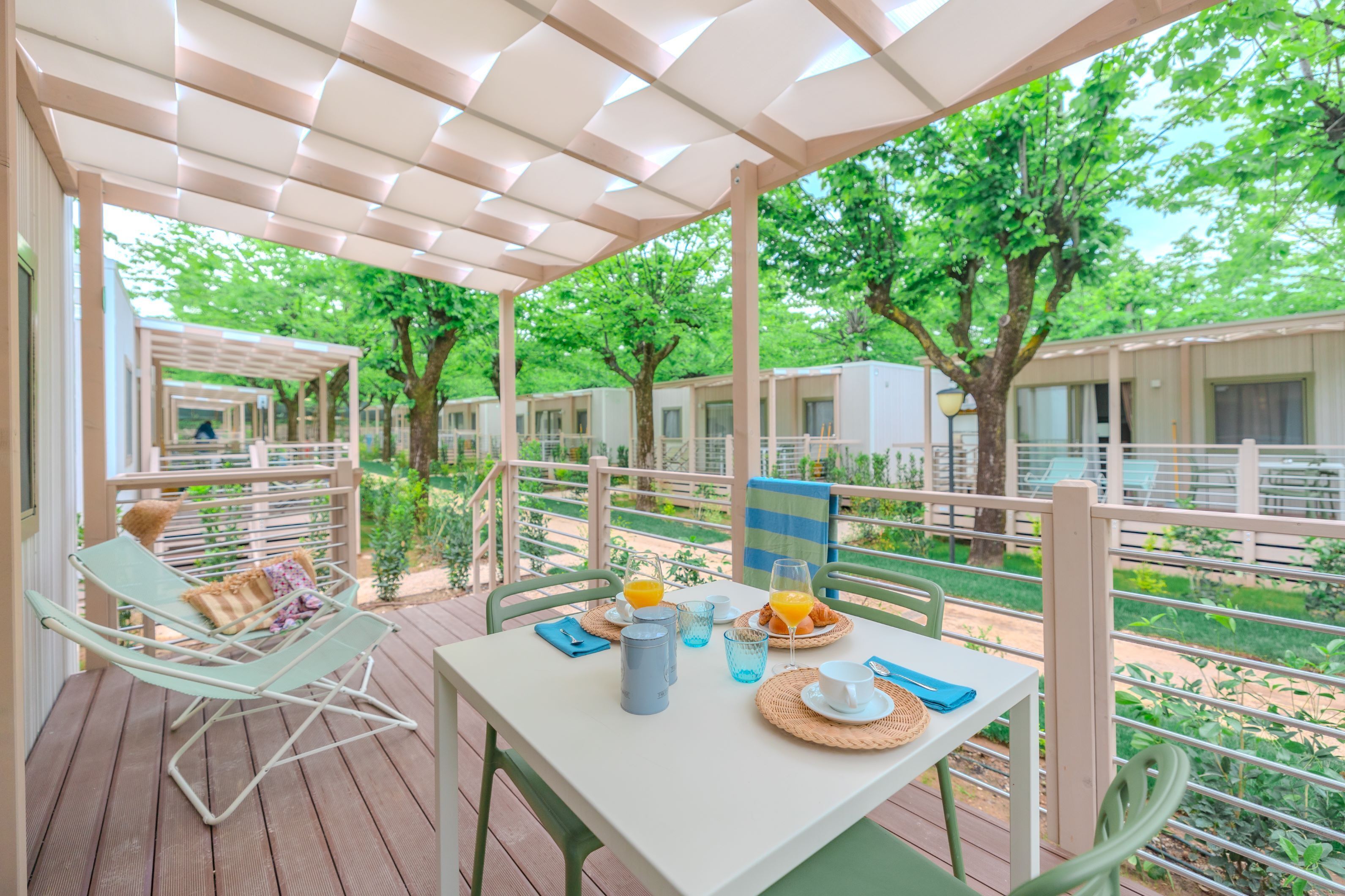 A covered outdoor dining area with a table set for breakfast, surrounded by greenery and trees.