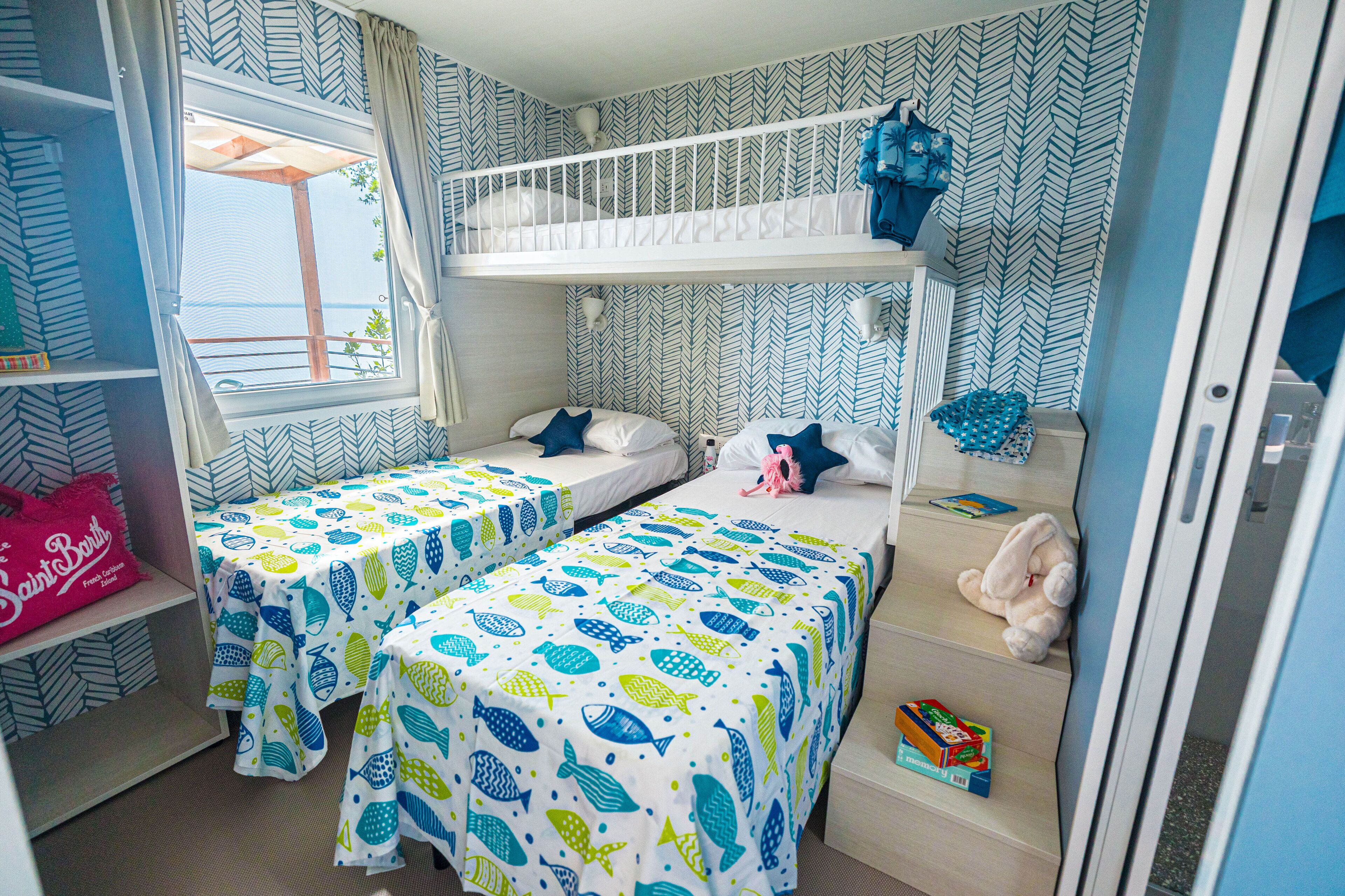 A children's room with bunk beds, two single beds, and a window with curtains.