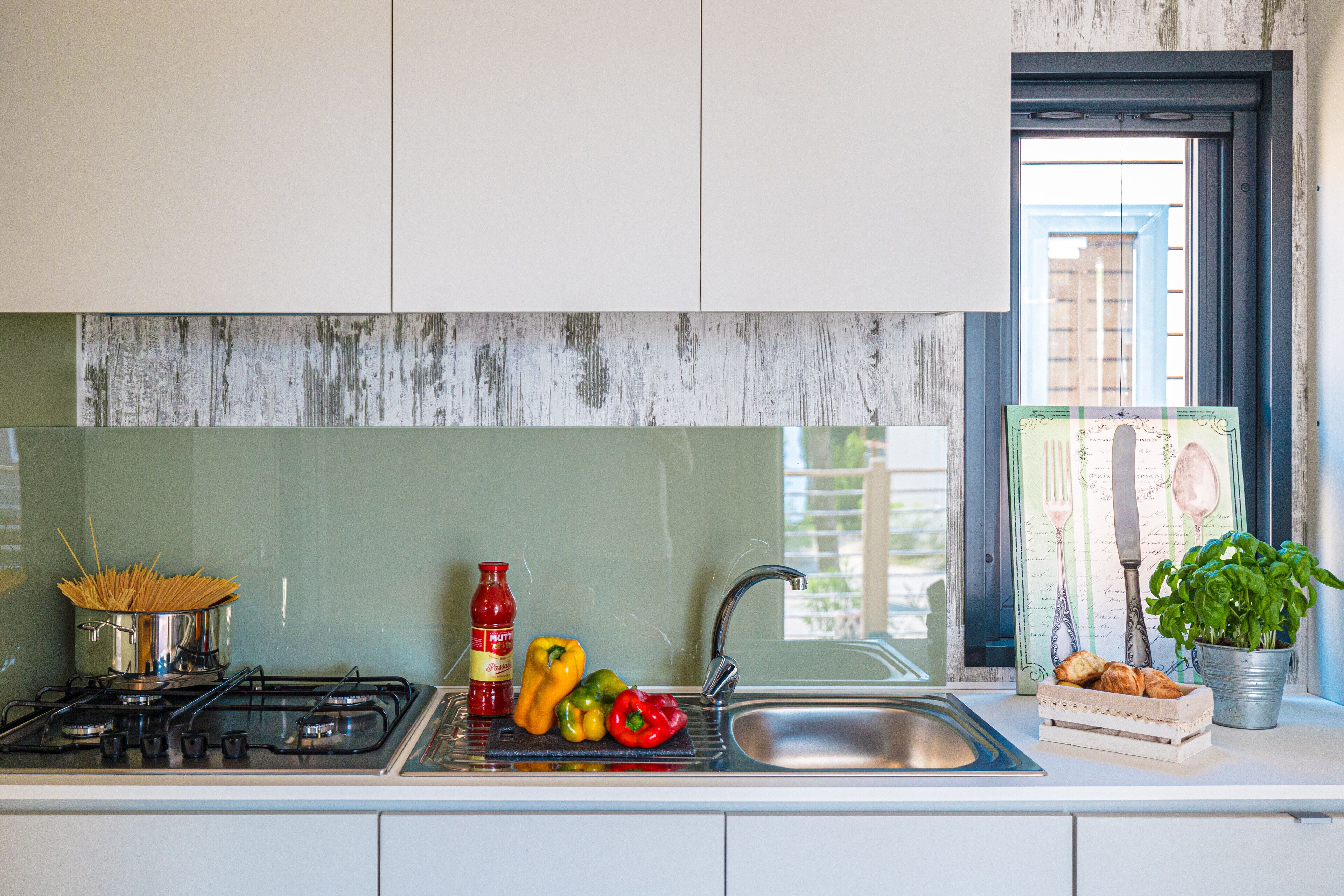 Una cocina con estufa, lavamanos y ventana con vista a edificios.