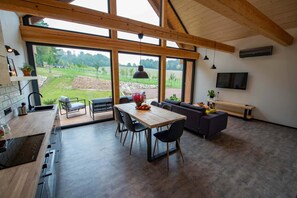 A modern kitchen with a dining area, large windows, and a TV.