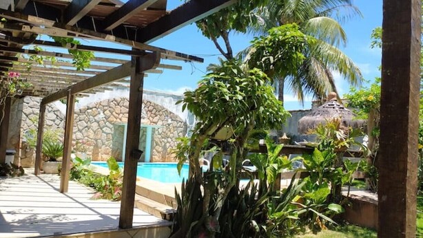 A covered outdoor area with a stone wall, a pool, and tropical plants. - House 6 bedrooms (4 suites) in Geribá with swimming pool (Cem Bracas Armação dos Búzios)