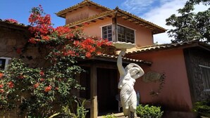 A house with a garden, including a statue and red flowers. - House 6 bedrooms (4 suites) in Geribá with swimming pool (Cem Bracas Armação dos Búzios)