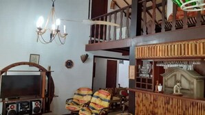 A room with a television, speakers, a chandelier, a clock, and a staircase leading to an upper level. - House 6 bedrooms (4 suites) in Geribá with swimming pool (Cem Bracas Armação dos Búzios)