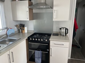 Kitchen features a stainless steel gas stove, oven, and range hood, along with a sink, coffee maker, and window with blinds.