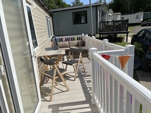 Relax on the deck with a wooden table, sofa, and chairs, surrounded by a white picket fence.