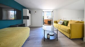 A modern living room with a yellow sofa, a glass coffee table, and a large TV mounted on a teal wall. - Cozy, new apartment in the historic center and 5 minutes from the beach (Forio)