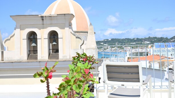 A rooftop terrace with a white chair, a small building with a dome, and a view of the sea and cityscape. - Cozy, new apartment in the historic center and 5 minutes from the beach (Forio)