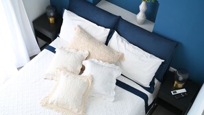 A neatly made bed with white and blue bedding, a bedside table with a lamp, and a small plant on the nightstand. - Cozy, new apartment in the historic center and 5 minutes from the beach (Forio)