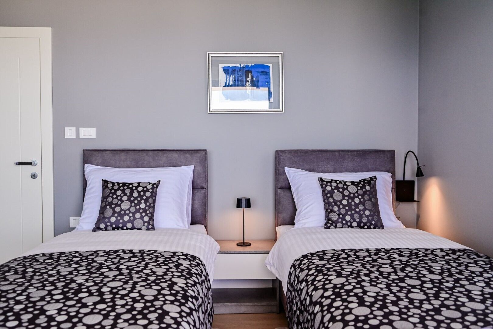 Habitación doble con dos camas, cada una con cubrecama de lunares, una obra de arte enmarcada sobre las camas y una mesita de noche con lámpara entre ellas.