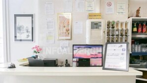 Una mesa de recepción con un monitor de computadora, diplomas enmarcados y un terminal de pago.