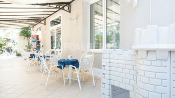 Un patio al aire libre con sillas y mesas de metal blanco, una chimenea de ladrillo y una zona de estar cubierta con techo metálico.