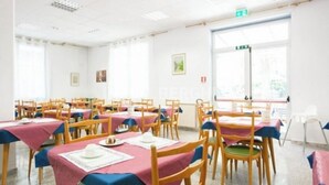 Comedor con mesas dispuestas para una comida, sillas y una ventana con persianas.