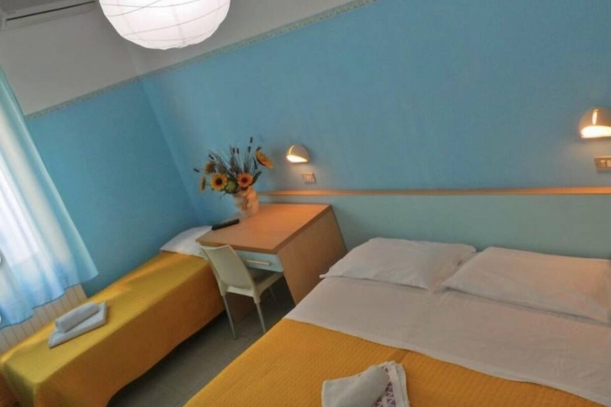 Habitación de hotel con dos camas, un escritorio, una silla y una lámpara colgante.