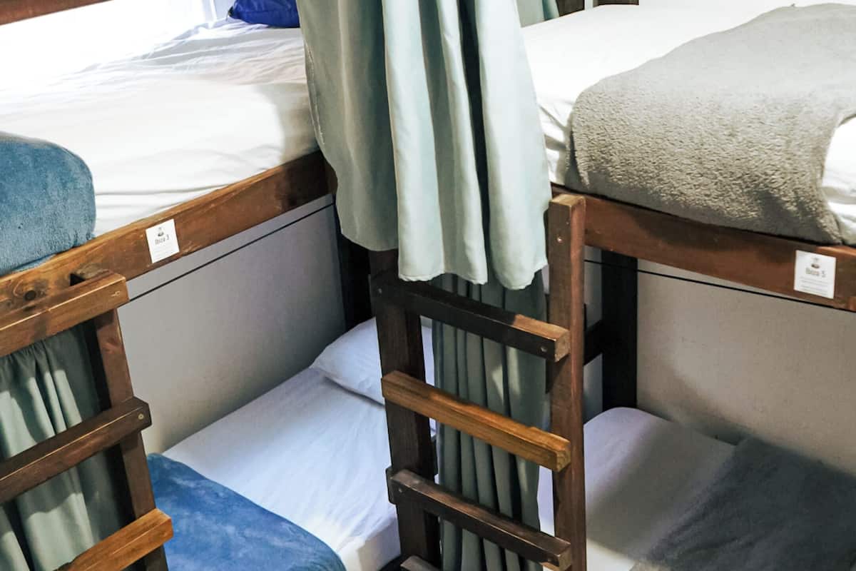 Uma cama beliche com escada, uma janela com cortinas e um colchão com etiqueta.