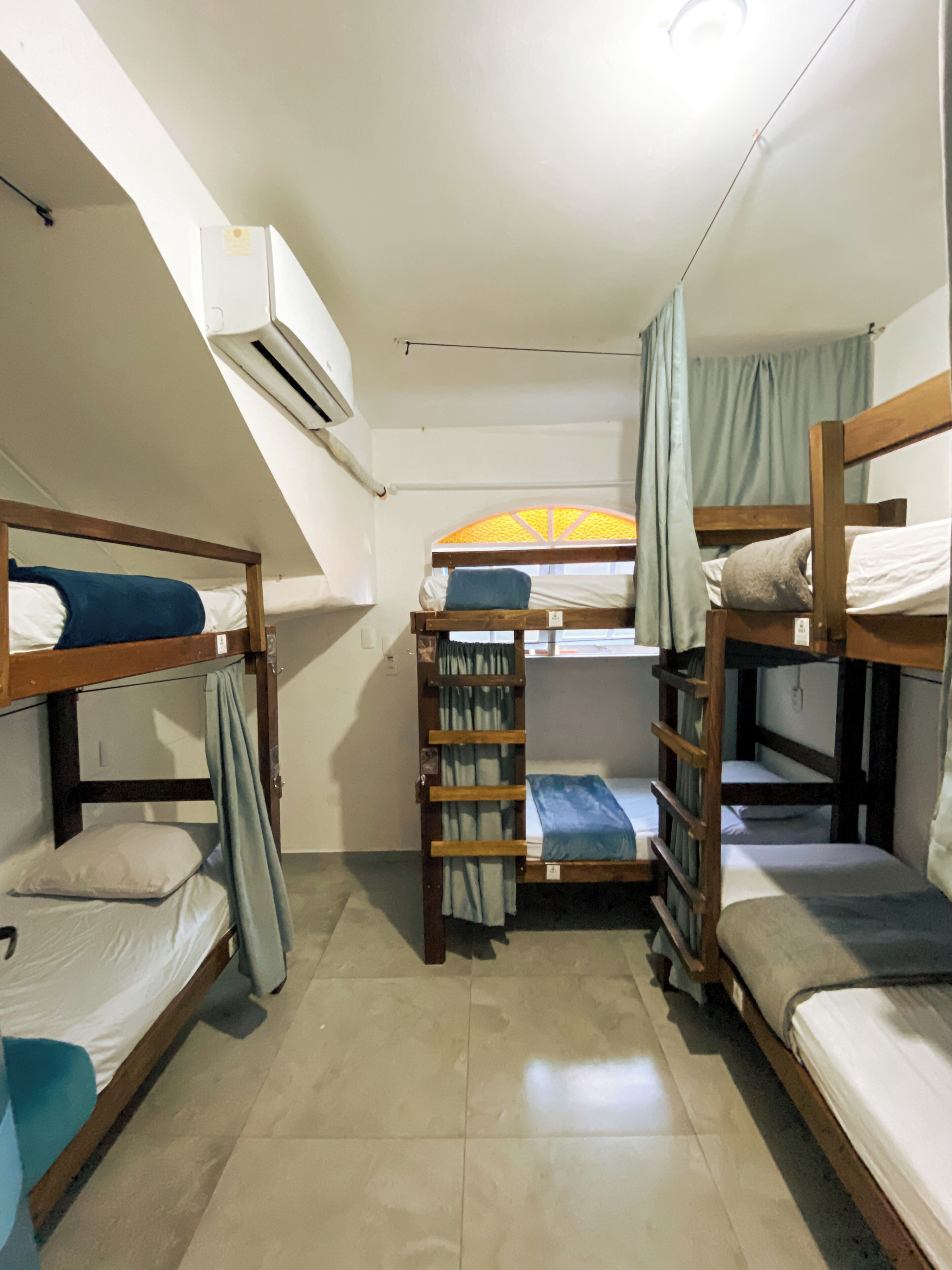 Un dormitorio con literas, una ventana con cortinas, un equipo de aire acondicionado y piso de baldosas.
