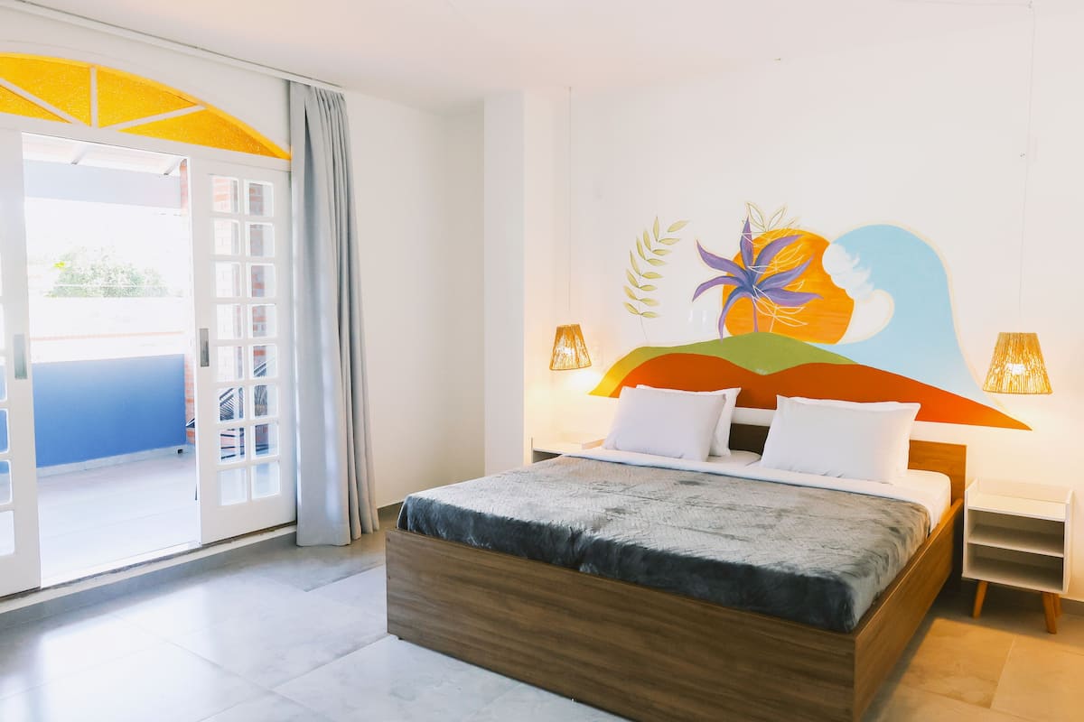 Quarto de hotel moderno com uma cama grande, uma varanda com vista e um mural na parede.