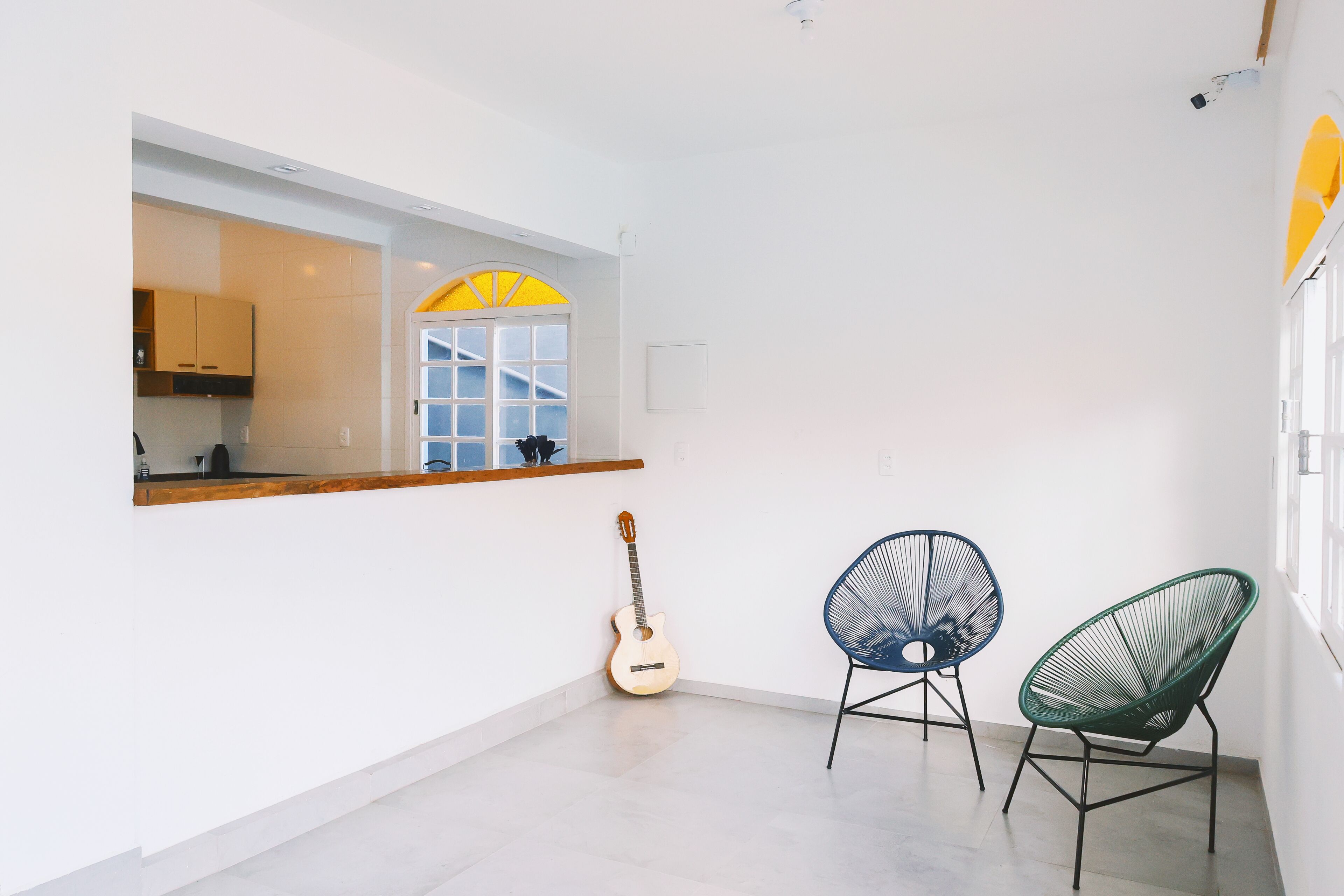 A bright, minimalist room with a large window, a wooden guitar, and two modern chairs.