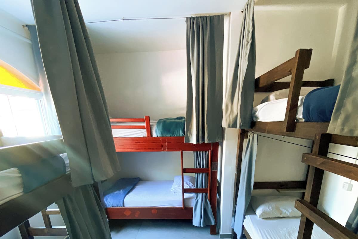 Um quarto de dormitório com beliches, ventilador de teto e cortinas.