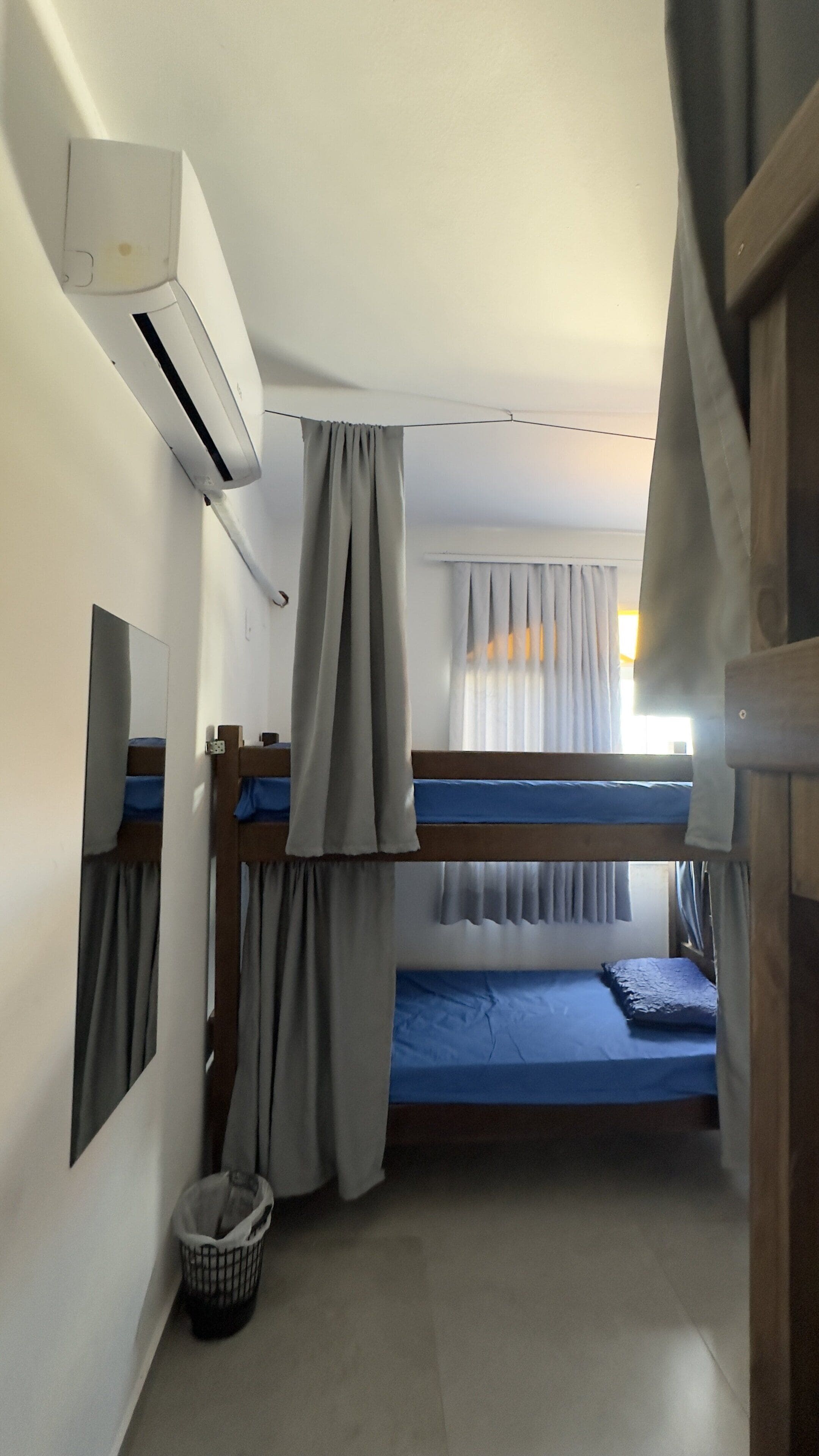 A room with bunk beds, an air conditioning unit, a mirror, and a window with curtains.