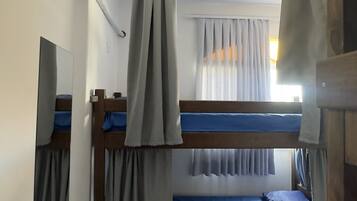 A room with bunk beds, an air conditioning unit, a mirror, and a window with curtains.