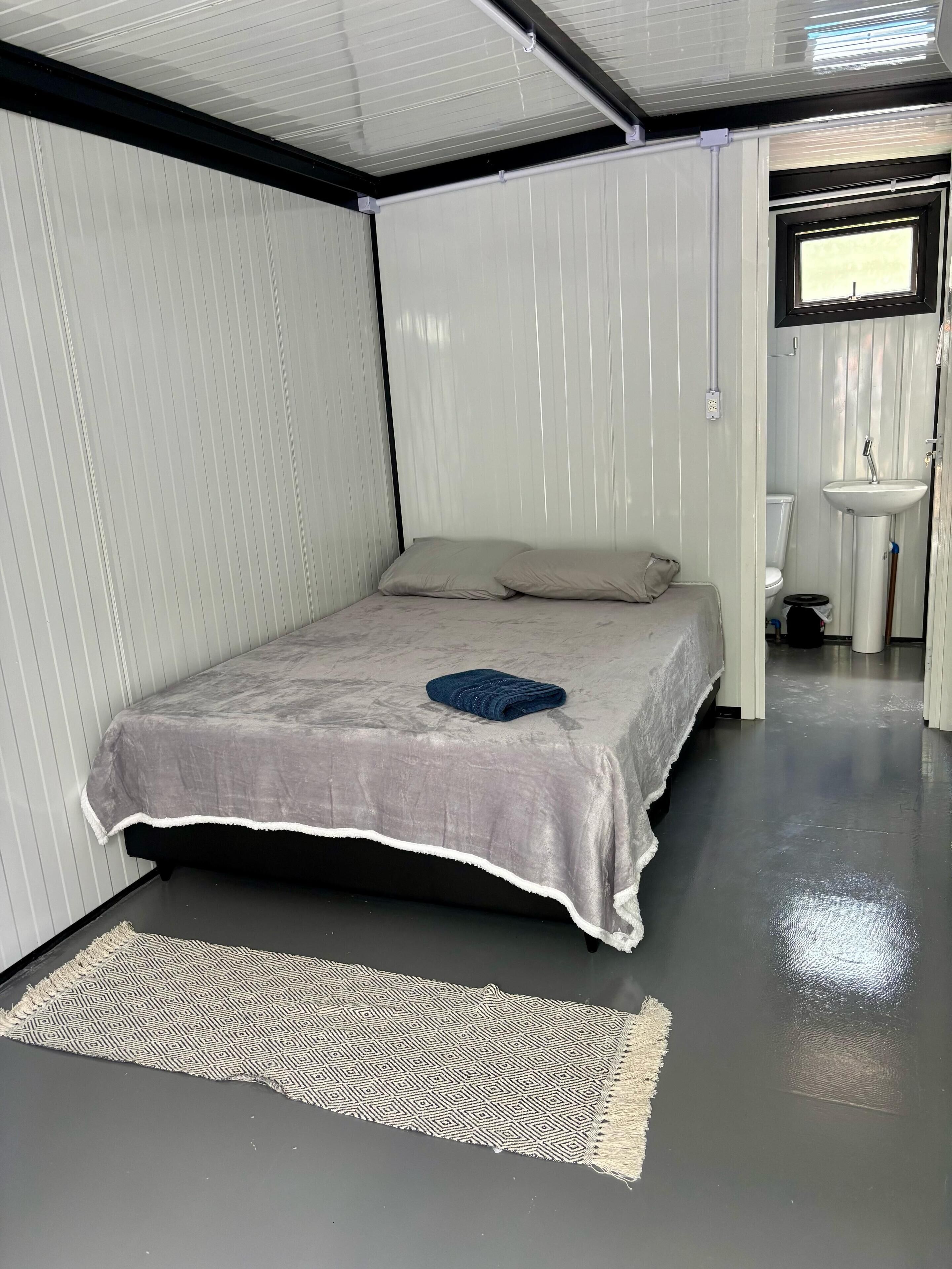 A compact bedroom with a bed, a bedside table, a patterned rug, and a window.