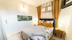 Un dormitorio con cama, mesita de noche, lámpara de pared y un cuadro.