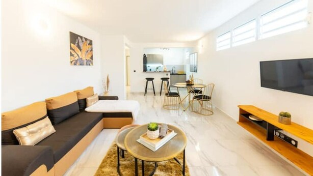 Una sala de estar moderna con un sofá, una mesa de centro y un televisor. Hay un comedor con sillas y una mesa.