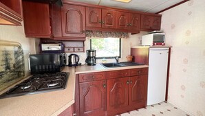 Een kleine keuken met houten kastjes, een gasfornuis, een koffiezetapparaat, een magnetron en een koelkast.