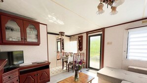 Een woonkamer met een houten tv-meubel, een eettafel met stoelen, een bank en een groot raam.